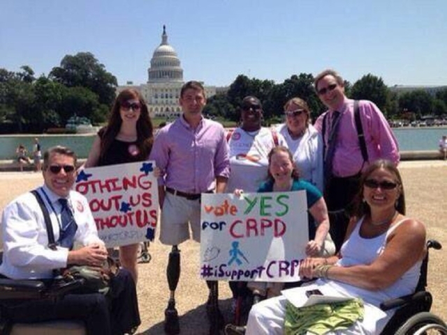 Group of CRPD leadership and advocates all with big signs in support of CRPD, in front of the U.S. Capitol and reflecting pond.