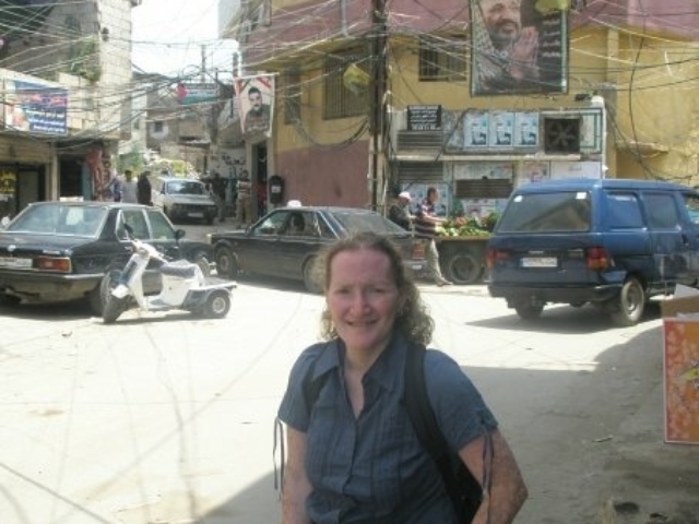 Rhonda visiting a Palestinian refugee camp and disability community. In fornt of a building with big signs and many electrical wires.