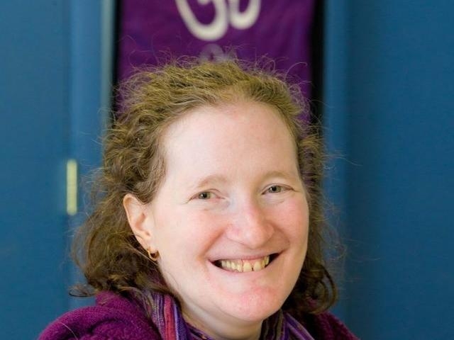 Rhonda wearing purple and a scarf with an Om symbol in background.