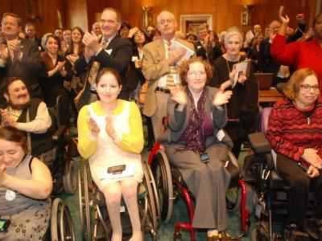 Advocates standing and sitting in wheelchairs clapping, smiling and cheering for the CRPD.