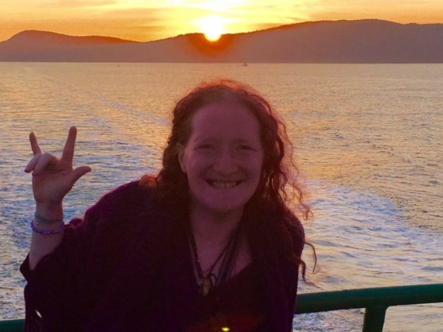 Rhonda giving an ASL "I love you" from a ferry over the water and sunset.