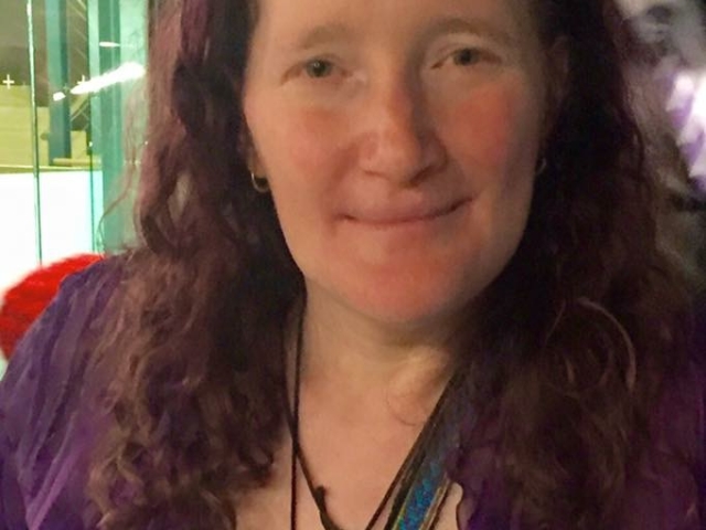 Rhonda looking at the camera wearing a purple shirt. COnference nametag on.