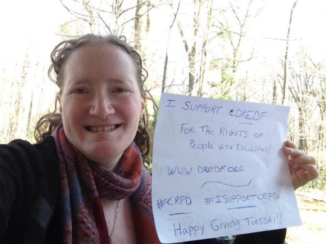 Rhonda holding a sign that says "I support @dredf for the rights of people with disabilties. www.DREDF.org. #CRPD #ISupportCRPD. Happy Giving Tuesday!"