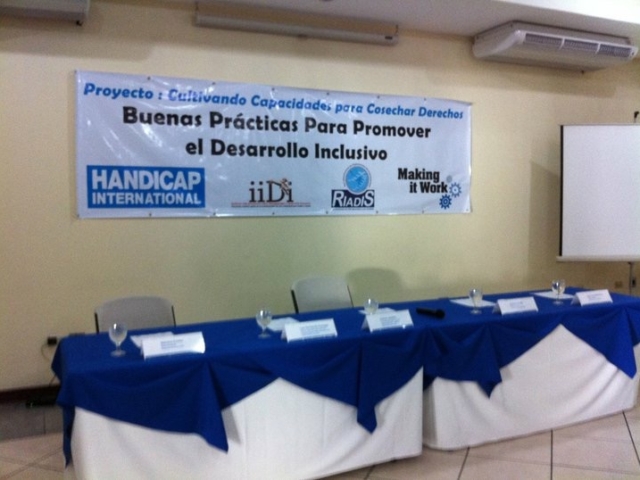 Empty and prepared panel for an event. Sign has the words in Spanish saying "Good Practices to Promote Inclusive Development" and organizational logos