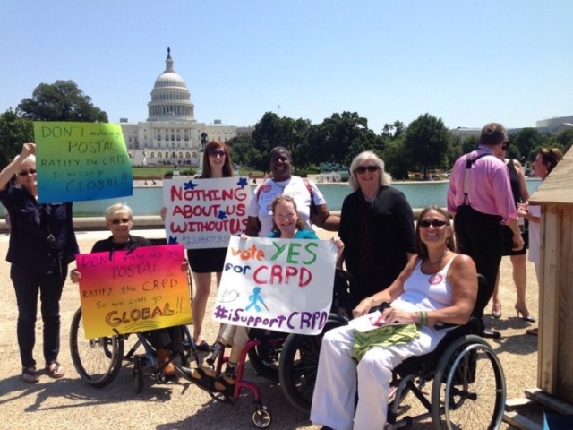 Group of CRPD leadership and advocates all with big signs in support of CRPD, in front of the U.S. Capitol and reflecting pond.