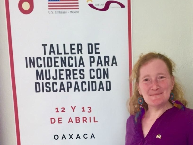 Rhonda standing next to a sign that reads "Taller de Incidencia para Mujeres con Discapacidad, 12 y 13 de Abril, Oaxaca (with sponsoring organizational logos).