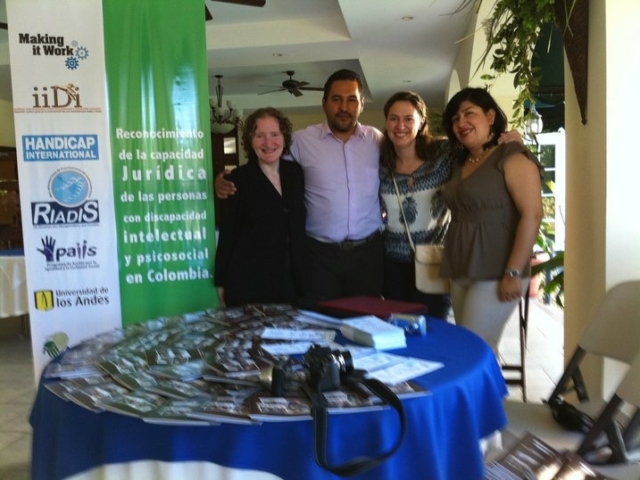 Rhonda and 3 colleagues in front of a table with materials, and a big banner with organizational logos and a project description in Spanish