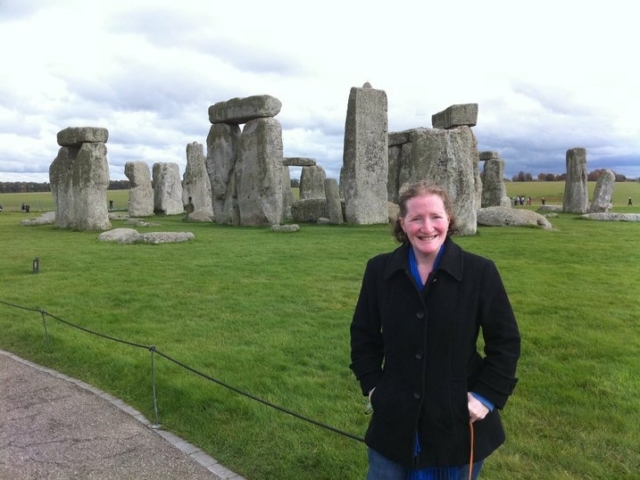 Rhonda in front of Stonehenge, wearing black coat.