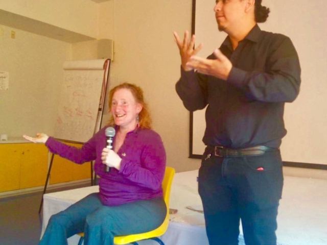 Rhonda training with microphone in hand. Sign language interpreter signing behind her