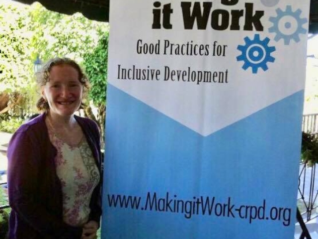 Rhonda standing beside a tall sign saying "Making it Work: Good Practices for Inclusive Development. www.MakingItWork-crpd.org