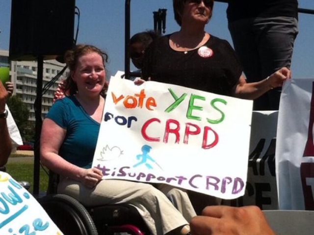 Rhonda sitting in her wheelchair holding a sign at CRPD rally saying "vote YES for CRPD #isupportCRPD"