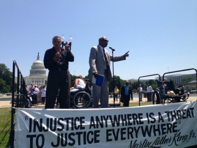 Wade Henderson of LCCHR speaking on stage at rally in front of US Capitol. Sign says "Injustice anywhere is a threat to justice everywhere" - MLK