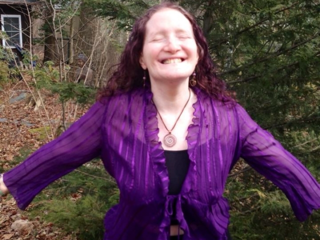 Rhonda wearing a purple shirt has her arms outstretched in joy, smiling at camera.